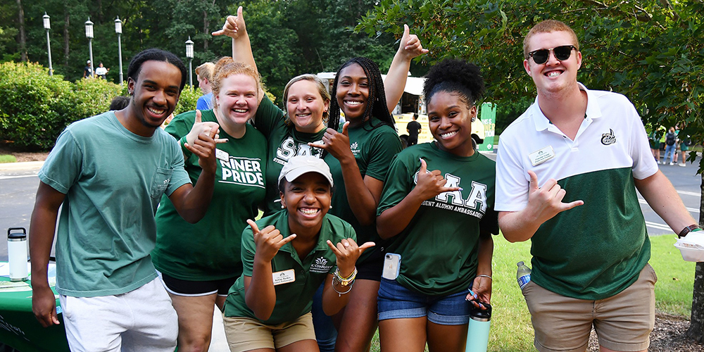 group of diverse UNC Charlotte students flashing the pick-axe sign