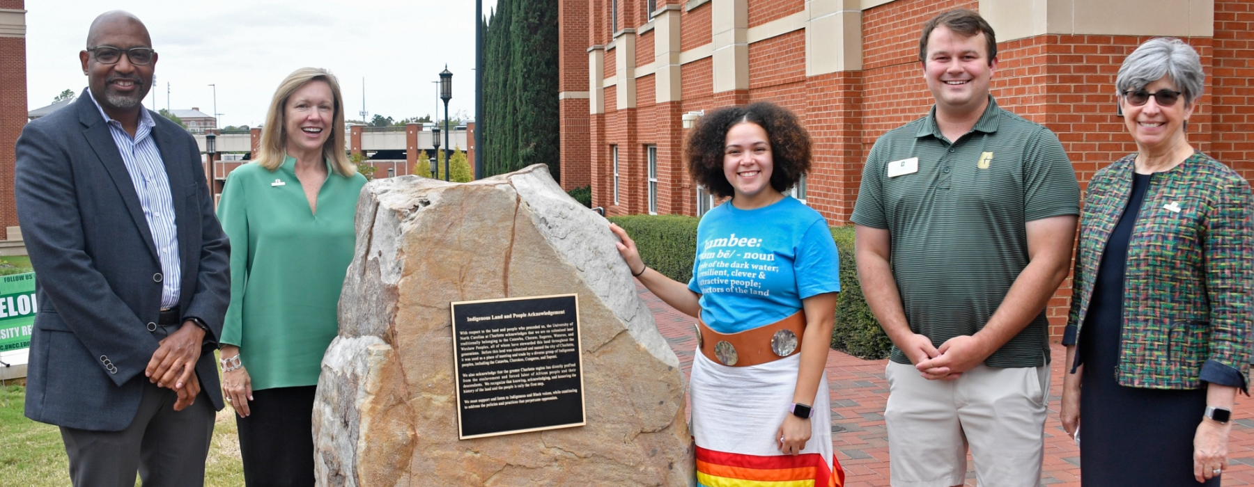 picture shows a group of University staff and students, including Chancellor Gaber and Native American Student Association President Page Freeman standing around the Land and People Acknowledgement plaque